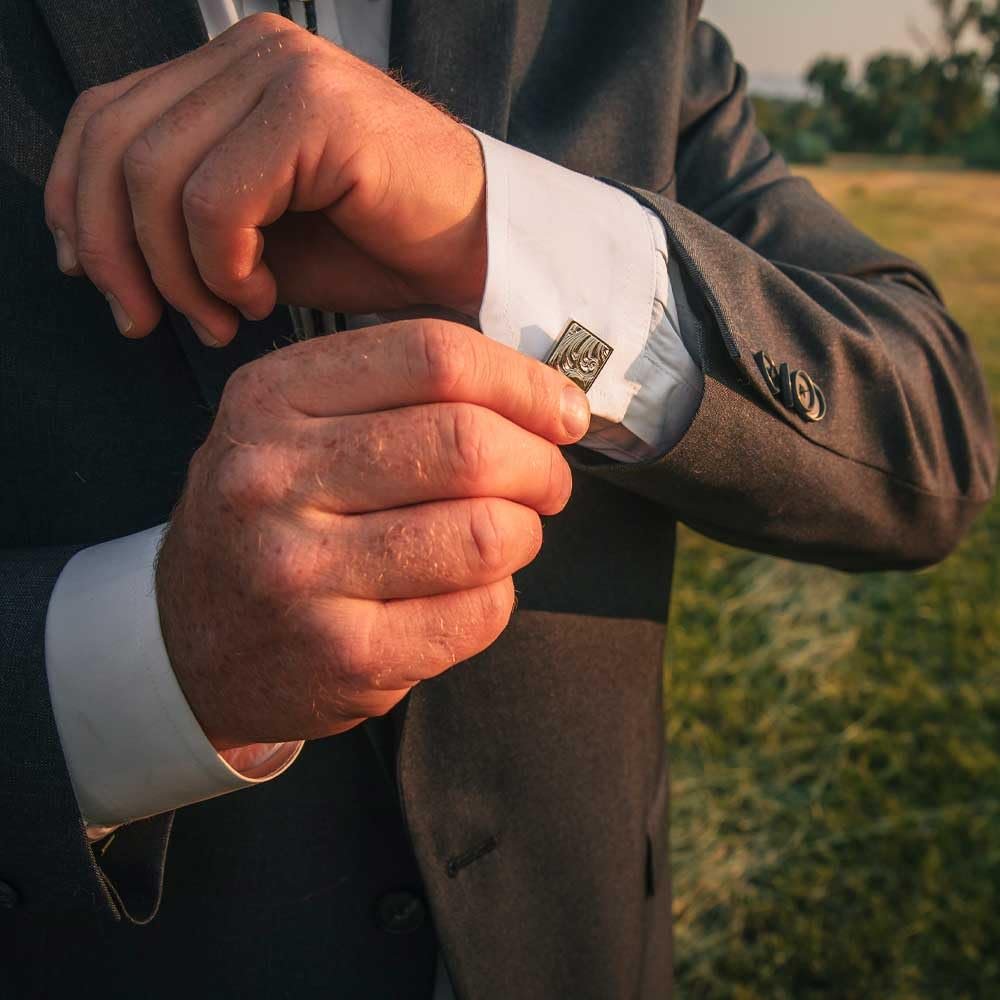 A man in a suit fastening his shirt cuffs with western cufflinks, adding a refined cowboy touch.