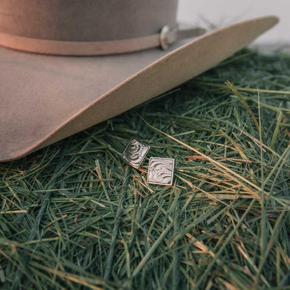Cufflinks resting on fresh grass beside a cowboy hat, embodying western elegance.