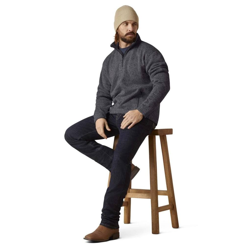 
                  
                    Man sitting on a wooden stool wearing a gray sweater, dark jeans, and a beige beanie.
                  
                