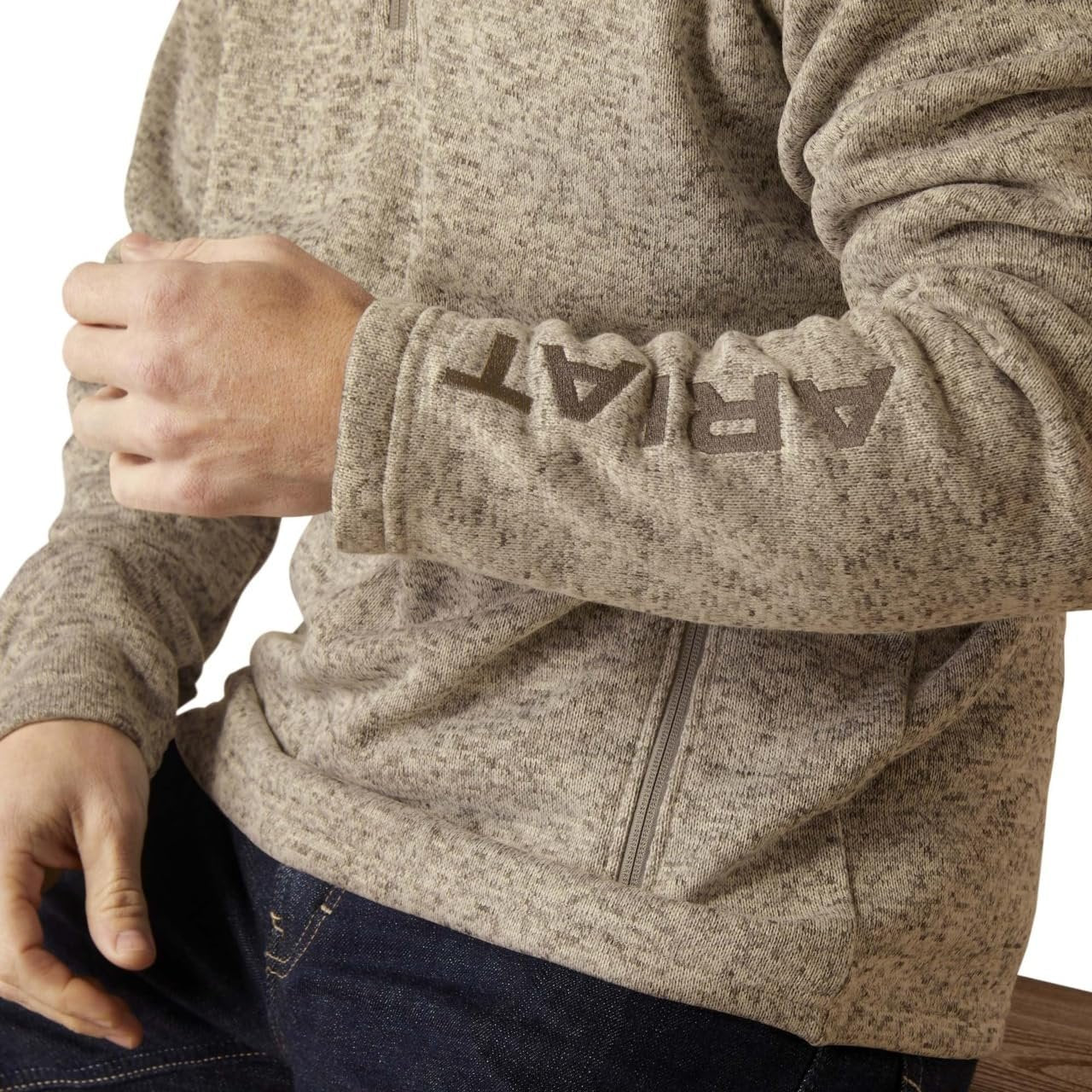 Close-up of a person wearing a beige fleece jacket with a brand logo on the sleeve.