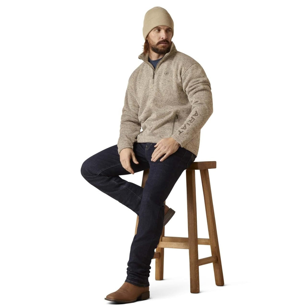 
                  
                    Man sitting on a wooden stool wearing a beige sweater, dark jeans, and brown boots on a white background.
                  
                
