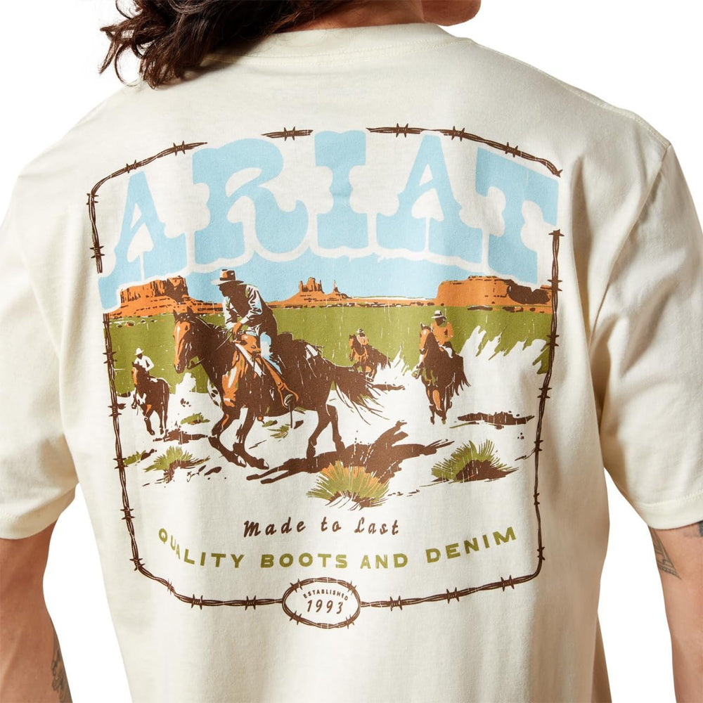 Beige t-shirt with ARIAT branding and graphic of cowboys on horses in a desert landscape.