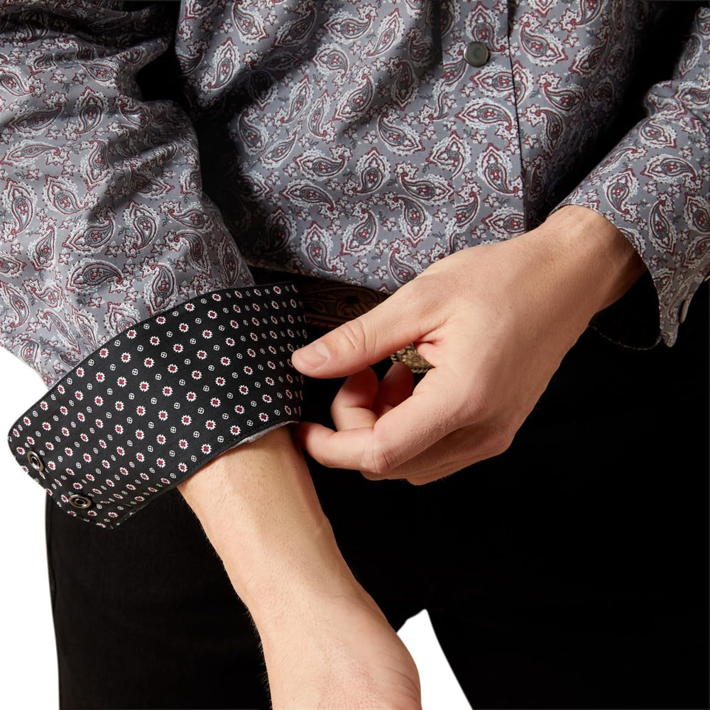 
                  
                    Person wearing a patterned shirt with rolled-up sleeves, adjusting a cuff.
                  
                