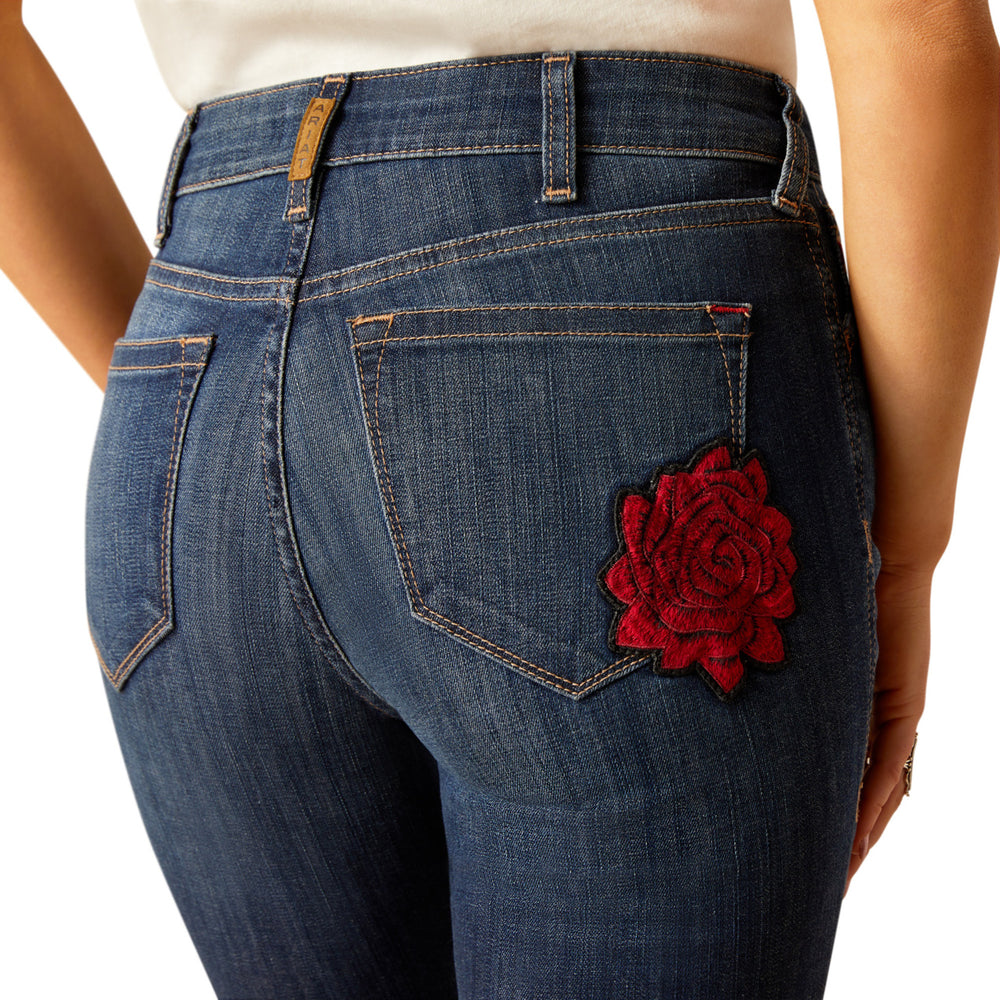 
                  
                    Blue jeans with a red floral patch on the pocket against a white background
                  
                