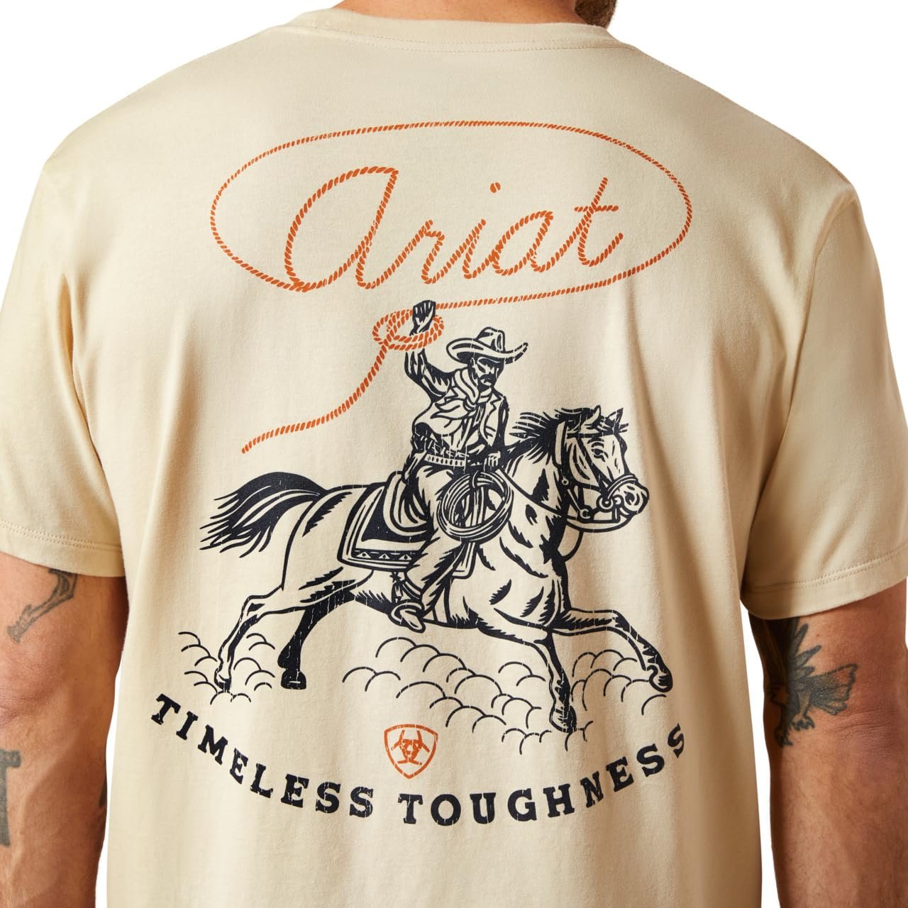 Beige t-shirt with a graphic of a cowboy on a horse and 'Ariat Timeless Toughness' text.