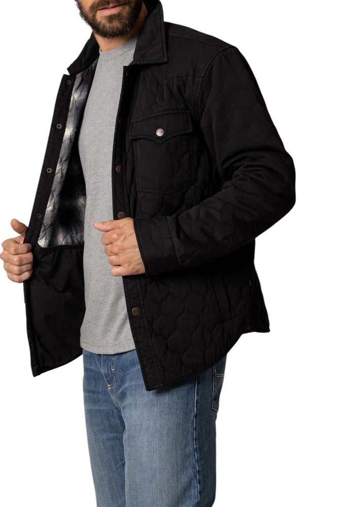 
                  
                    Man wearing a black quilted jacket over a gray shirt and blue jeans on a white background
                  
                