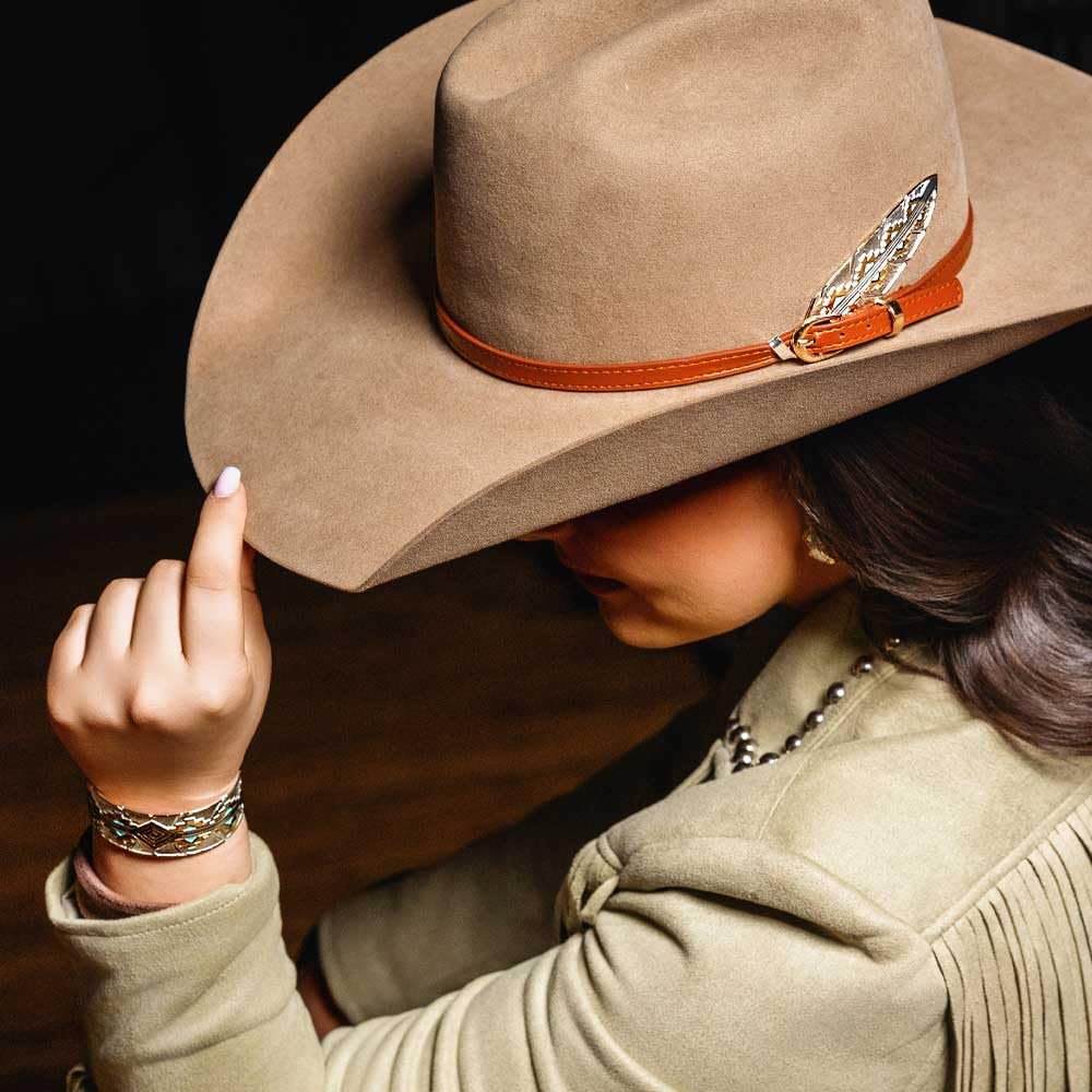 
                  
                    Person wearing a brown cowboy hat with a decorative band, adjusting it with one hand.
                  
                