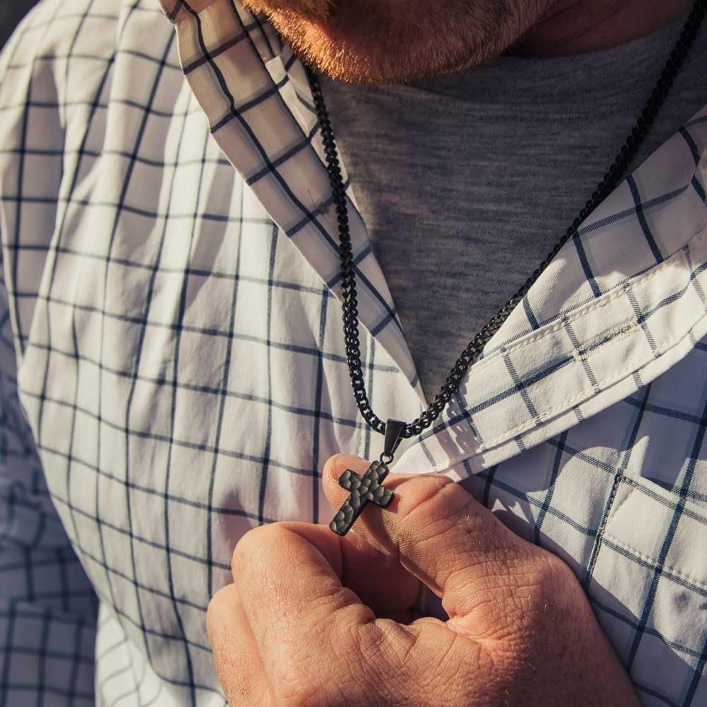 
                  
                    Person wearing a plaid shirt holding a black cross necklace.
                  
                
