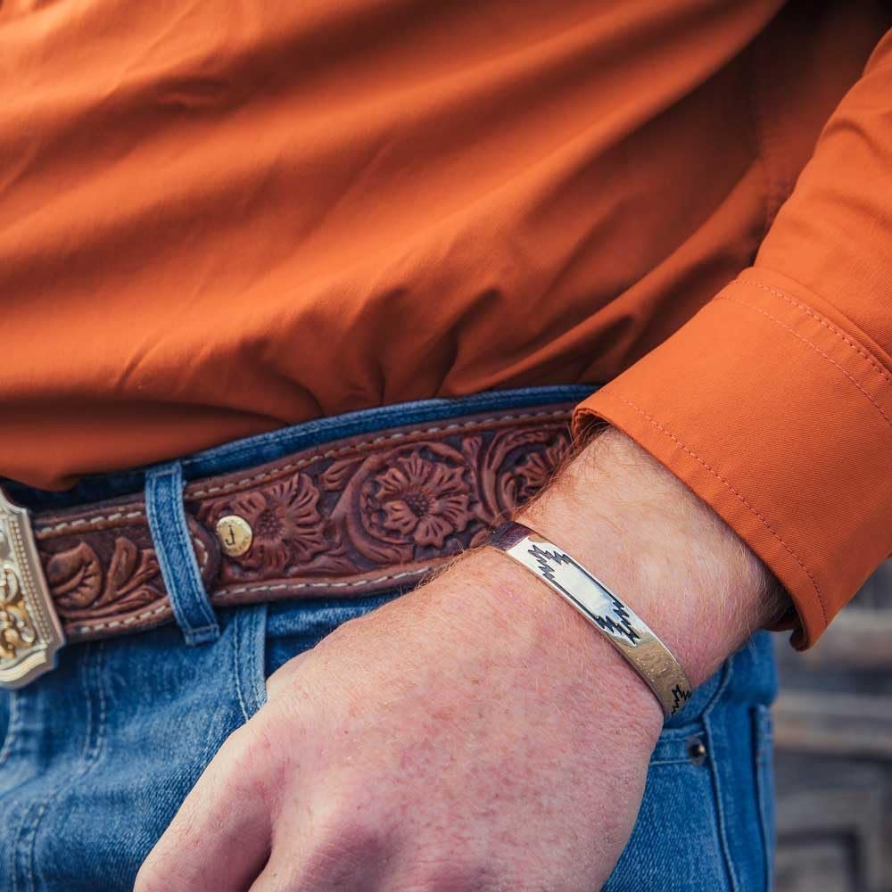 
                  
                    Person wearing an orange jacket with a brown leather belt and blue jeans, holding a metal bracelet.
                  
                