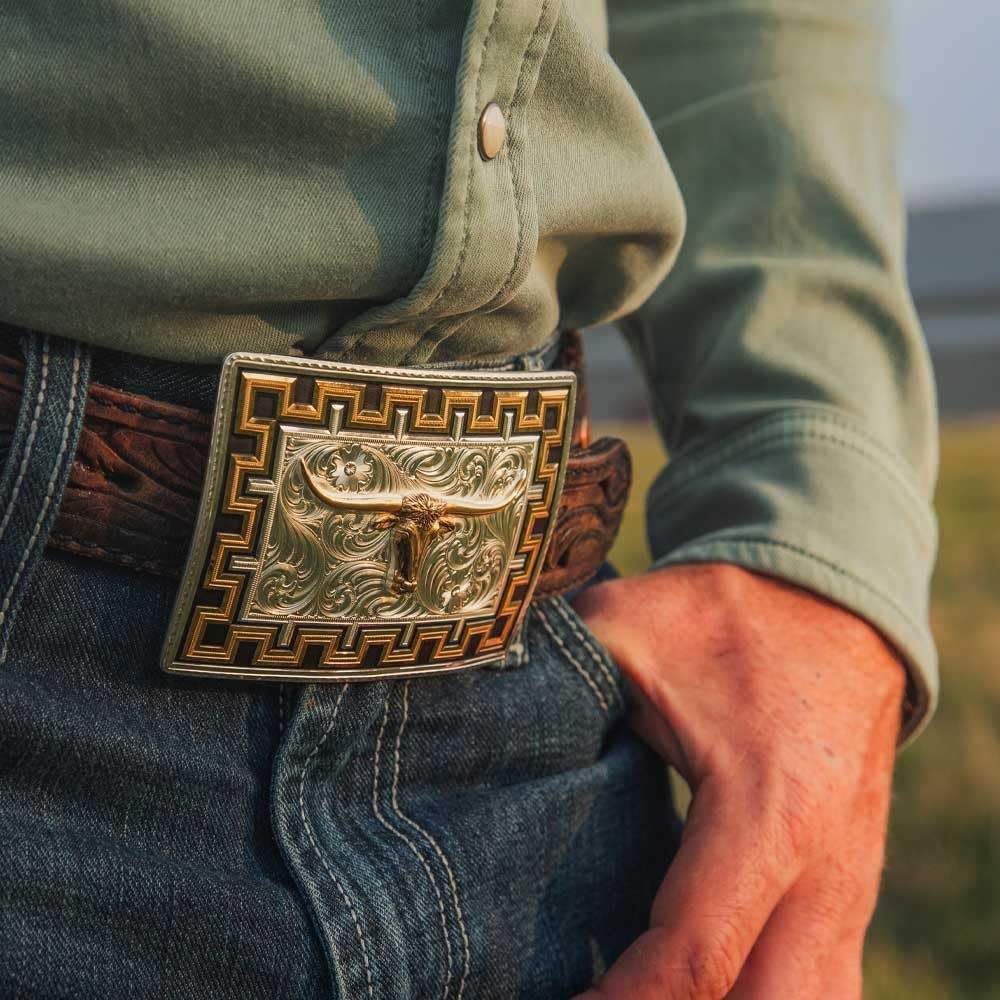 Close-up of a person wearing a green shirt and blue jeans with a decorative belt buckle.