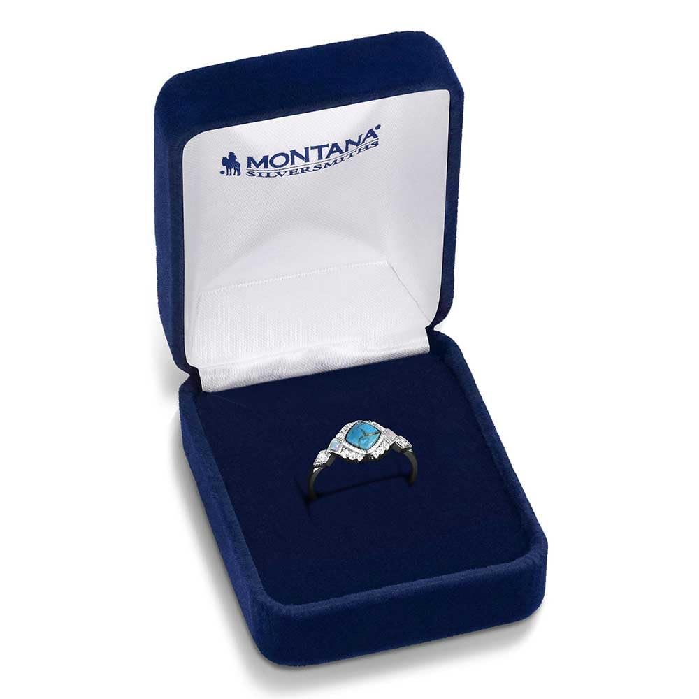 
                  
                    Blue velvet jewelry box with a silver ring featuring a blue gemstone on a white background, branded 'Montana Silversmiths'.
                  
                
