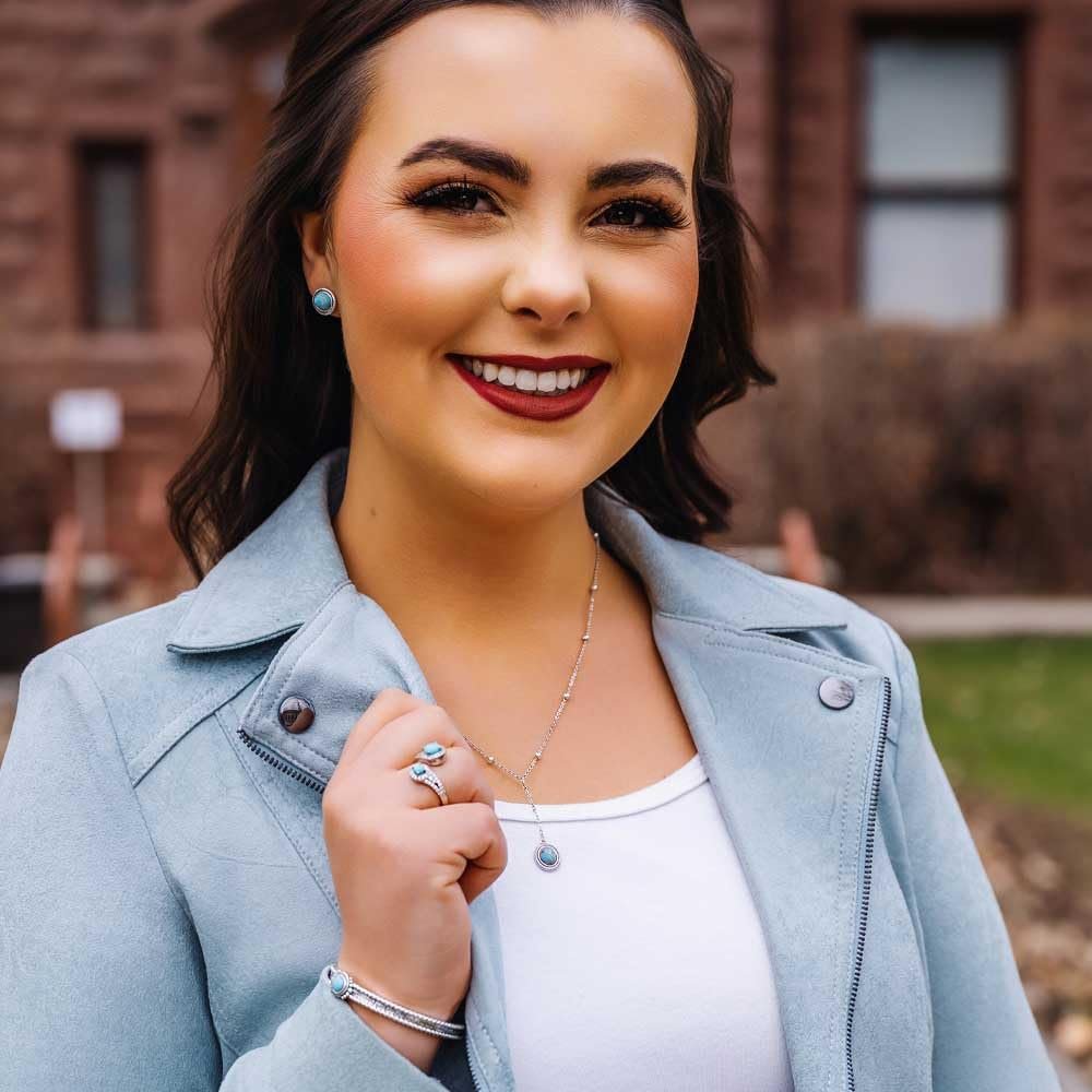 Woman wearing a light blue jacket and white top, standing outdoors with a blurred background