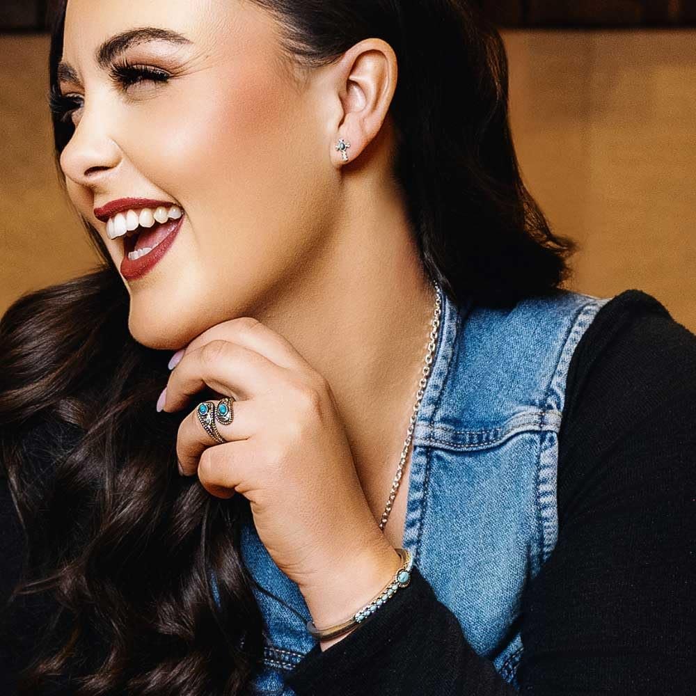 Woman wearing a denim vest with jewelry, smiling.
