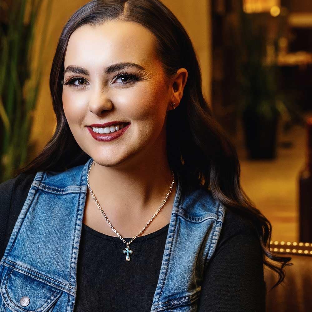 
                  
                    Woman wearing a denim jacket and black top with a blurred indoor background
                  
                