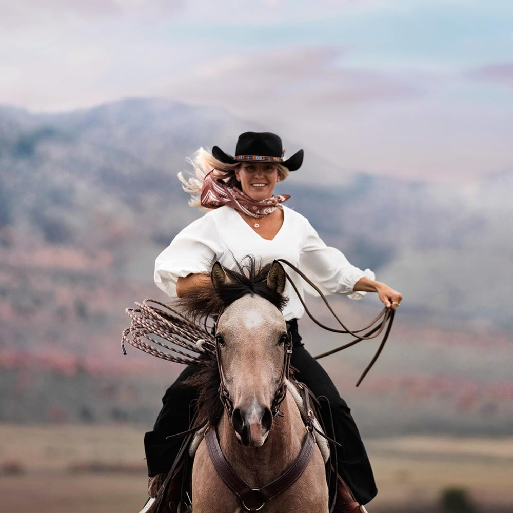 
                  
                    Cowgirl Wearing a Black Western Hat and White Long Sleeve Shirt, Riding a Horse Against Western Background
                  
                
