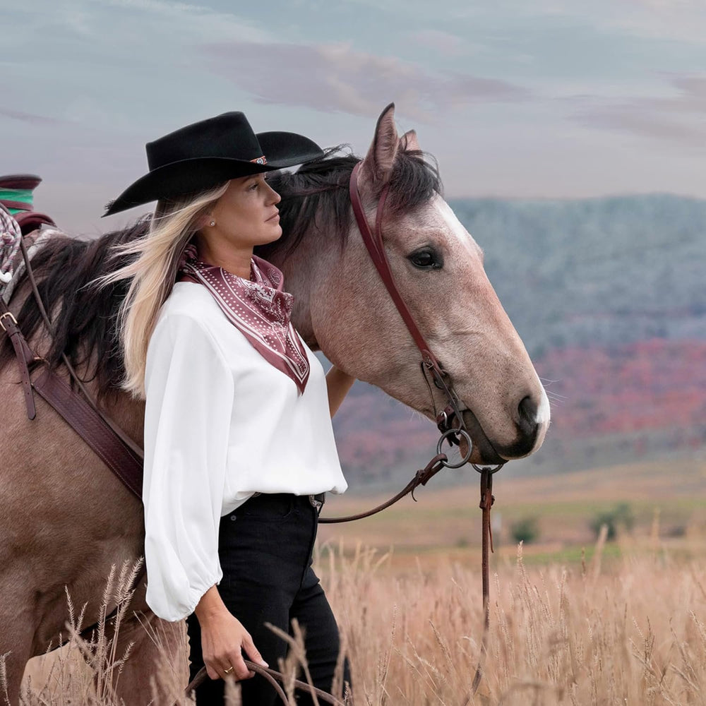 
                  
                    Cowgirl Wearing a Black Western Hat and White Long Sleeve Shirt, Standing by Her Horse Against Western Background
                  
                
