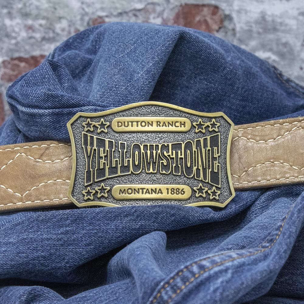 
                  
                    Montana Silversmiths x Yellowstone Collection Belt Buckle, With Dutton Ranch Yellowstone Montana Engraving Against Belt and Denim Fabric Background
                  
                